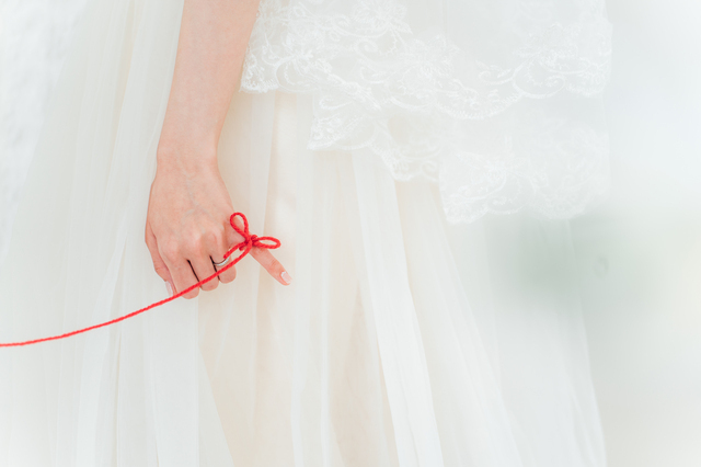 結婚式場で赤い糸で結ばれる新郎新婦の画像